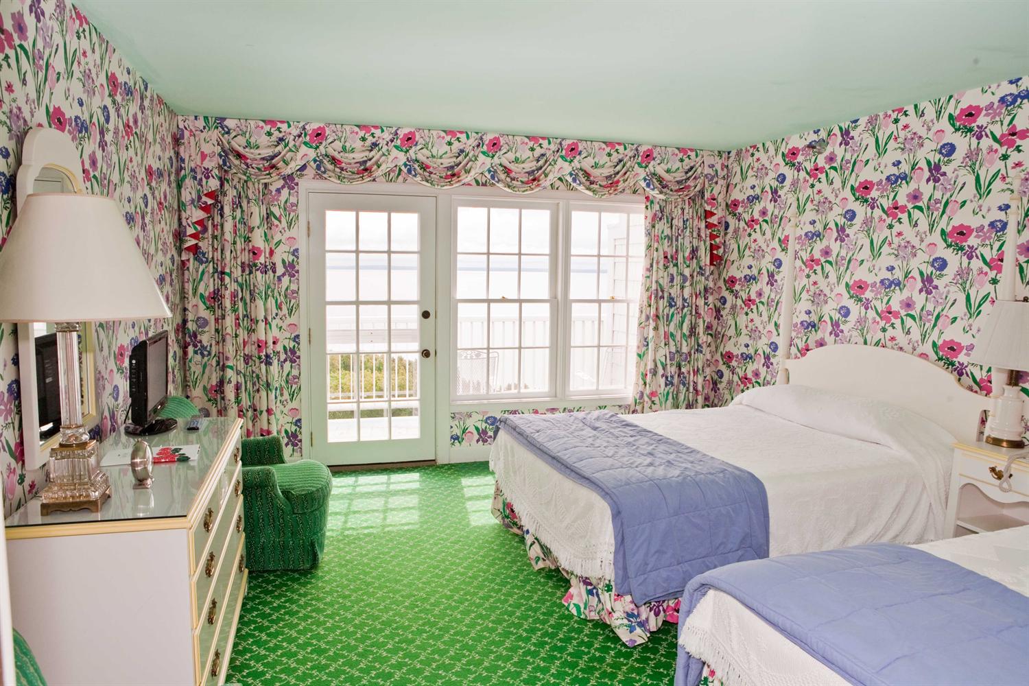 Image of Grand Room with floral painted wallpaper and two double beds with purple covers. Grand Hotel, a member of Historic Hotels since 2001, dates to 1886. It is located in Mackinac Island, Michigan.